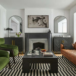 Contemporary living room with black and white stripe rug hunter green velvet accent chairs black cement coffee table and cognac leather tufted sofa