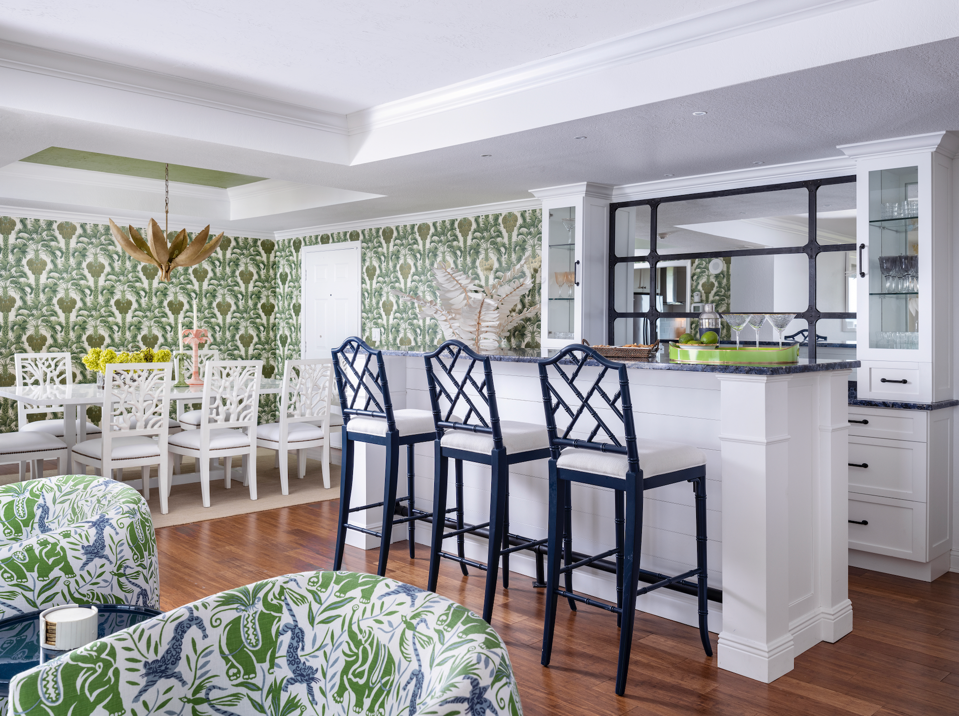 Green hollywood palm wallpaper with coral style dining chairs and gold palm chandelier Naples Florida home colorful playful style decor navy blue lacquer counter stools Chippendale style